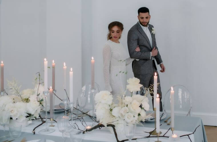 A wedding couple walking past and looking at a table decorated with candles and white blooms
