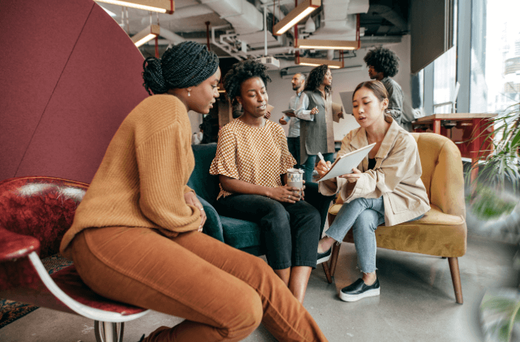 Three women, one with a pad and pen sitting and talking